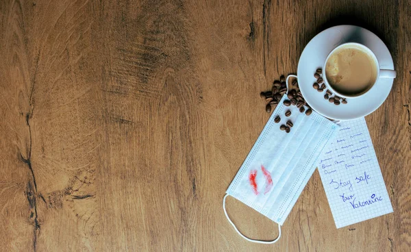 Sevgililer Günü aşk notu, kahve ve cerrahi koruyucu maske kahverengi, ahşap bir masada kahve çekirdekleri her yere dökülmüş. Sürpriz not, sevgililer gününü ayrı kalırken sevgiyi, ilgiyi ve kutlamayı gösteriyor..