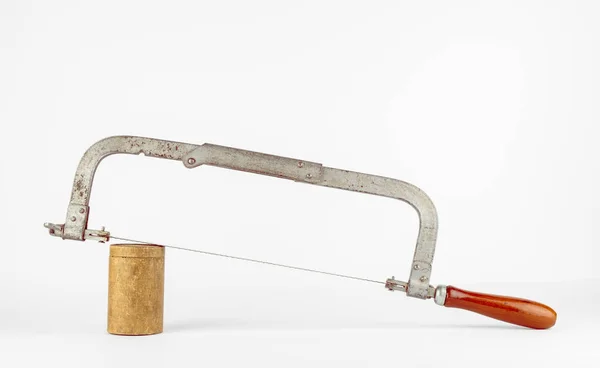 Yuvarlak bir tahta bloğa yerleştirilmiş eski paslı tahta testeresi. El testeresinin kahverengi ahşap sapı var..