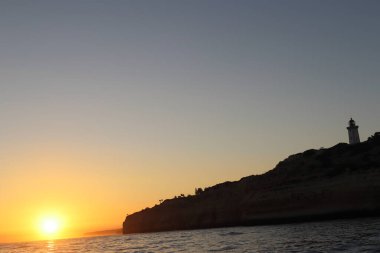 Tarihi Cabo de Sao Vicente Deniz feneri silueti Portekiz 'in Algarve kıyısındaki uçurumlarda dururken Atlantik Okyanusu üzerinde dramatik bir günbatımı yaşanıyor. Batan güneş, su ve gökyüzüne altın bir parıltı saçarak güzel ve huzurlu bir hava yaratıyor.