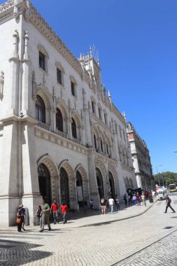 Lizbon 'un günlük yaşamını ve mimari mirasını yansıtan sokak düzeyinde bir editör fotoğrafı. Görüntü, Esta o de Caminhos de Ferro do Rossio 'dan geçen yayaları ve turistleri gösteriyor. Bu, 19. yüzyılın eşsiz at nalıyla bilinen bir simgesidir.