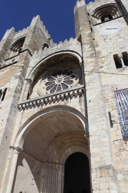 Şehrin en eski kilisesi olan Lisboa Lizbon Katedrali 'nin düşük açılı mimari çekimi. Fotoğraf, etkileyici Roma kireç taşı cephesini, büyük merkezi gül penceresini ve güçlü ortaçağ çan kulelerini vurguluyor.