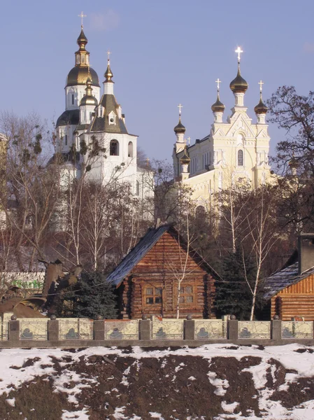 Бревенчатые дома и монастырь на заснеженном холме на фоне гор — стоковое фото