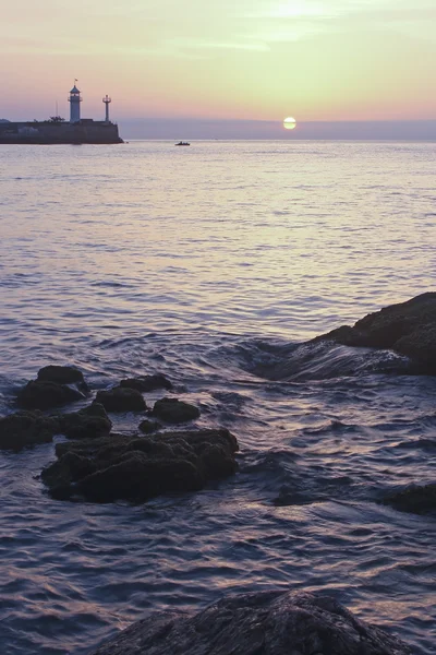 Arka planda deniz feneri ile denize gündoğumu