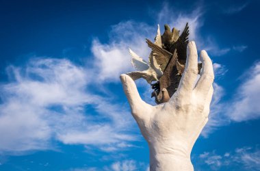 Türkiye 'nin Kusadasi kentindeki heykel, arka planda parçalı bulutlu yaz gökyüzü ile farklı renklerdeki kuşları serbest bırakan bir eli temsil ediyor