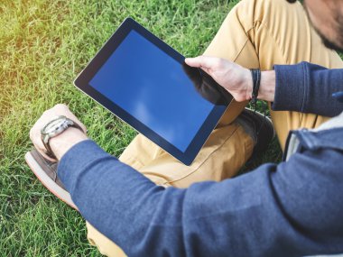 Adamın elleri parkta çim üzerinde oturan bir dijital Tablet Mockup kullanarak