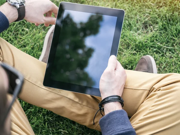 Männerhände mit einer digitalen Tablet-Attrappe mit weißem Bildschirm, die auf dem Gras im Park sitzt — Stockfoto