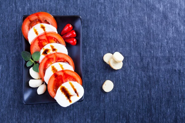 Tomate e mussarela, prato preto, desenho, hortelã, biscoitos finos, molho — Fotografia de Stock