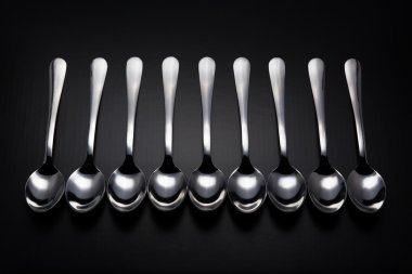Siyah arka plan üzerine dokuz paslanmaz çelik kaşık.