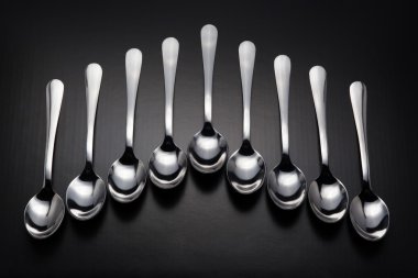 Siyah arka plan üzerine dokuz paslanmaz çelik kaşık. Ok