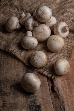 Tahta bir masa ve çuval bezi üzerinde taze mantarlar. Fotoğraf stüdyosu ışıklandırması sebze yemeği. Sümbül kutusunda düğme mantarları