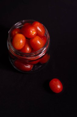 Cam kavanozdaki taze vişneli domateslerin sade fotoğrafı. Siyah arka planda izole edilmiş cam bir kavanozda kiraz domateslerinin koyu renkli fotoğrafı..