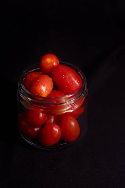 Cam kavanozdaki taze vişneli domateslerin sade fotoğrafı. Siyah arka planda izole edilmiş cam bir kavanozda kiraz domateslerinin koyu renkli fotoğrafı..