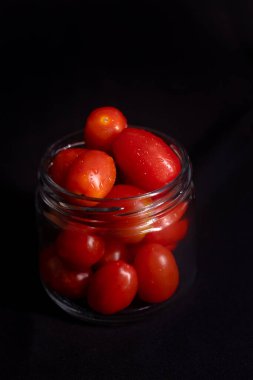 Cam kavanozdaki taze vişneli domateslerin sade fotoğrafı. Siyah arka planda izole edilmiş cam bir kavanozda kiraz domateslerinin koyu renkli fotoğrafı..