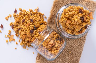 Cam kavanozda granola ve beyaz arka plan. Kavanozdan granola dökülüyor.