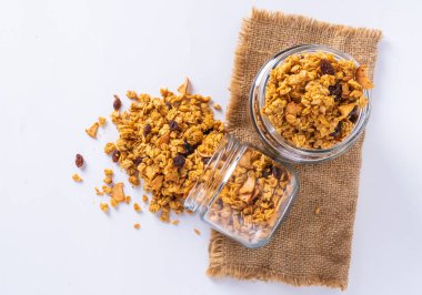 Cam kavanozda granola ve beyaz arka plan. Kavanozdan granola dökülüyor.