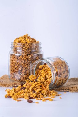 Cam kavanozda granola ve beyaz arka plan. Kavanozdan granola dökülüyor.