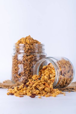 Cam kavanozda granola ve beyaz arka plan. Kavanozdan granola dökülüyor.
