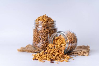 Cam kavanozda granola ve beyaz arka plan. Kavanozdan granola dökülüyor.