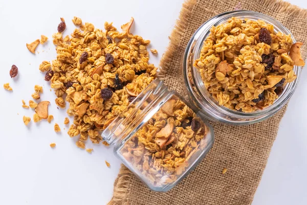 Cam kavanozda granola ve beyaz arka plan. Kavanozdan granola dökülüyor.