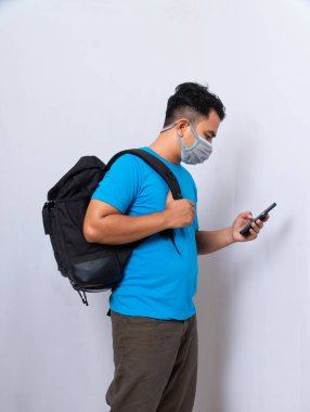 Siyah sırt çantalı bir adam, kovid 19 virüsünden korunmak için tıbbi maske ve bez bir maske takıyor. Maskeli ve sırt çantalı bir adam aramak için cep telefonu kullanmış.