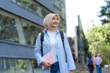 Mavi ceket ve pembe kitap giyen genç bir kadın caddede yürüyor. Gülümsüyor ve mutlu.