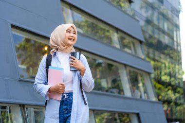 Mavi gömlek ve beyaz gömlek giyen genç bir kadın bir cep telefonu ve bir kitap tutuyor. Gülümsüyor ve mutlu.