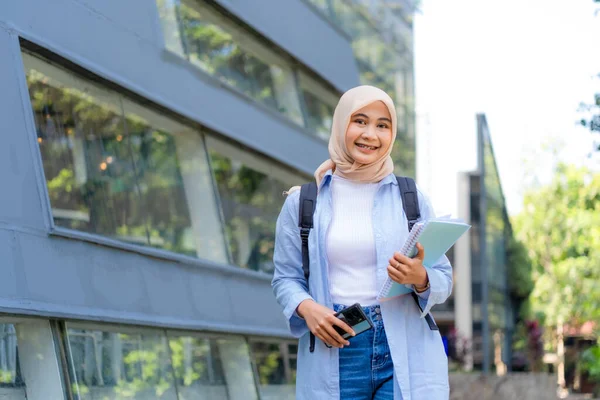 Mavi gömlek ve beyaz gömlek giyen genç bir kadın bir cep telefonu ve bir kitap tutuyor. Gülümsüyor ve mutlu.