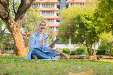Bir üniversite öğrencisi, modern yaşam tarzını ve dijital eğitim eğilimlerini gösteren tabletini bir park ortamında İnternet üzerinden öğrenmeyi seviyor.