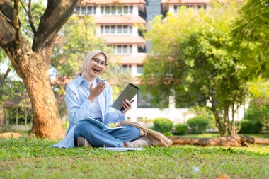 Bir üniversite öğrencisi, modern yaşam tarzını ve dijital eğitim eğilimlerini gösteren tabletini bir park ortamında İnternet üzerinden öğrenmeyi seviyor.