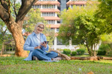 Bir üniversite öğrencisi, modern yaşam tarzını ve dijital eğitim eğilimlerini gösteren tabletini bir park ortamında İnternet üzerinden öğrenmeyi seviyor.