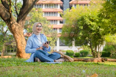 Bir üniversite öğrencisi, modern yaşam tarzını ve dijital eğitim eğilimlerini gösteren tabletini bir park ortamında İnternet üzerinden öğrenmeyi seviyor.
