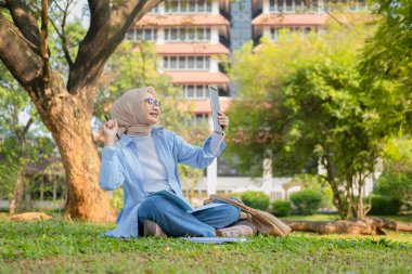 Bir üniversite öğrencisi, modern yaşam tarzını ve dijital eğitim eğilimlerini gösteren tabletini bir park ortamında İnternet üzerinden öğrenmeyi seviyor.
