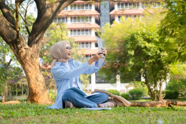 Bir üniversite öğrencisi, modern yaşam tarzını ve dijital eğitim eğilimlerini gösteren tabletini bir park ortamında İnternet üzerinden öğrenmeyi seviyor.