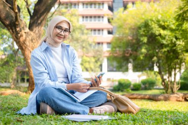 Bir üniversite öğrencisi, modern yaşam tarzını ve dijital eğitim eğilimlerini gösteren tabletini bir park ortamında İnternet üzerinden öğrenmeyi seviyor.