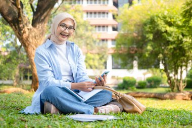 Bir üniversite öğrencisi, modern yaşam tarzını ve dijital eğitim eğilimlerini gösteren tabletini bir park ortamında İnternet üzerinden öğrenmeyi seviyor.