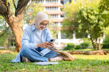 Genç bir Asyalı Müslüman kadın kampüsünün çimlerinde ya da halka açık bir parkta oturuyor. Cep telefonundaki bilgilere sevinçle tepki veriyor. Kolu zafer ve heyecan dolu bir jestle havada..