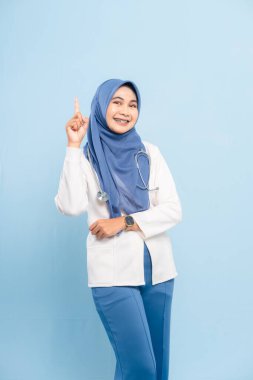 Asyalı genç Müslüman doktor ya da hemşirenin portresi açık elle sunuluyor, kopya alanı veya mavi arka planda izole edilmiş önemli bir şeyi gösteriyor..