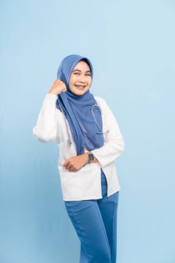 Kendinden emin bir Asyalı Müslüman doktor ya da hemşirenin portresi güçlü ya da kararlı, mavi arka planda izole bir şekilde gülümsüyor..