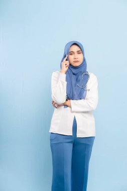 Endişeli bir Asyalı Müslüman doktorun ya da hemşirenin portresi derin düşünen, mavi bir arka plan izole etti..