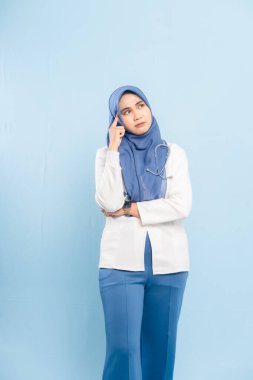 Endişeli bir Asyalı Müslüman doktorun ya da hemşirenin portresi derin düşünen, mavi bir arka plan izole etti..