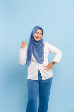 Kendine güvenen bir Asyalı Müslüman doktor ya da hemşirenin portresi güçlü ya da kararlı, mavi bir arkaplana gülümsüyor..