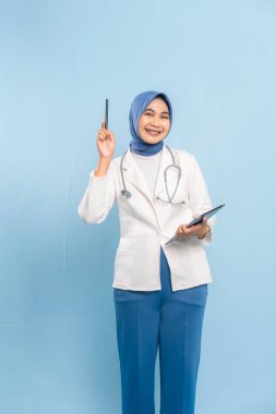 Dijital Tableti işaret eden Asyalı Müslüman Doktor veya Hemşire Tıbbi Bilgileri Vurguluyor. Mavi arkaplanda izole edilmiş