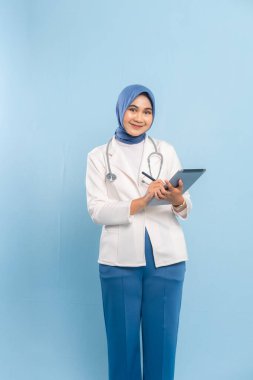 Gülümseyen Asyalı Müslüman Doktor veya Dijital Tablet üzerinde çalışan Hemşire. Mavi arkaplanda izole edilmiş