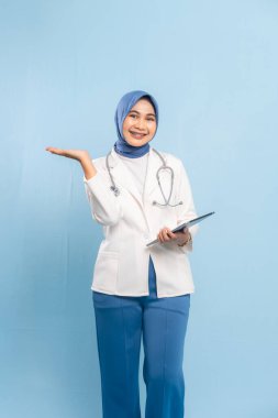 Dijital Tableti işaret eden Asyalı Müslüman Doktor veya Hemşire Tıbbi Bilgileri Vurguluyor. Mavi arkaplanda izole edilmiş