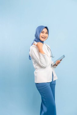 Dijital Tableti işaret eden Asyalı Müslüman Doktor veya Hemşire Tıbbi Bilgileri Vurguluyor. Mavi arkaplanda izole edilmiş