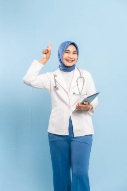 Dijital Tableti işaret eden Asyalı Müslüman Doktor veya Hemşire Tıbbi Bilgileri Vurguluyor. Mavi arkaplanda izole edilmiş