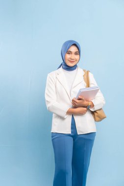 Gülümseyen ve kendinden emin genç bayan tıp öğrencisi ya da tesettürdeki doktor. Mavi arkaplanda izole edilmiş.