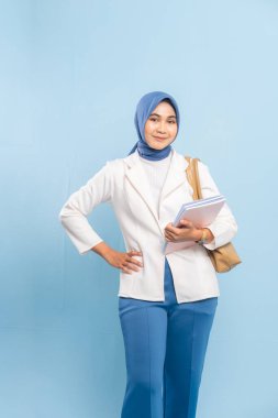 Gülümseyen ve kendinden emin genç bayan tıp öğrencisi ya da tesettürdeki doktor. Mavi arkaplanda izole edilmiş.