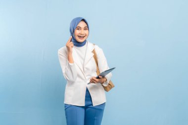 Düşünceli ya da kafası karışmış Asyalı genç Müslüman ya da elinde tablet tutarken bir fikri düşünen öğrenci. Mavi bir arkaplanda izole edilmiş.