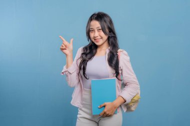 Bir kadın elinde mavi bir kitap tutuyor ve önemli bir şeye işaret ediyor. Gülümsüyor ve mutlu.